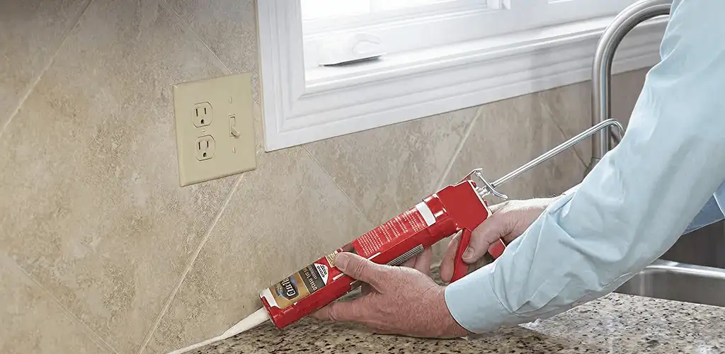 Handyman applying caulk along a kitchen backsplash and countertop seam in Naperville, IL